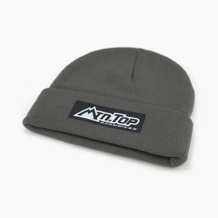 A dark gray knit beanie hat with a folded cuff, featuring a black rectangular patch on the front with the white text 'MTN.TOP Snowbikes' and a mountain graphic.