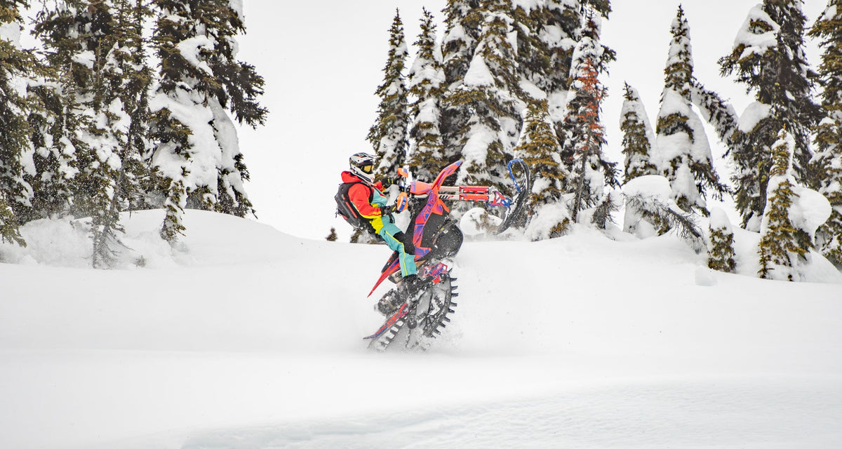 Person on a snowbike in a snowy forest popping a wheelie